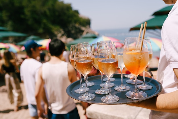 Een ober met een dienblad in de hand draagt cocktails en drankjes op een feestje op het strand een sinaasappelcocktail