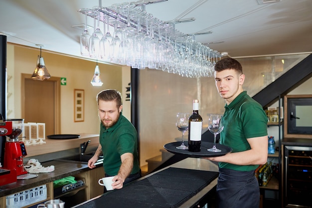 Een ober met een dienblad met fles wijn en glazen in het restaurant van de bar-pub.