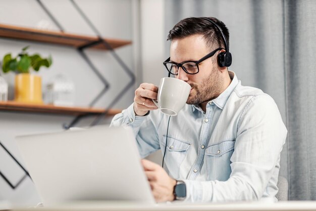 Een ondernemer die koffie drinkt en videobelt op de laptop in zijn thuiskantoor