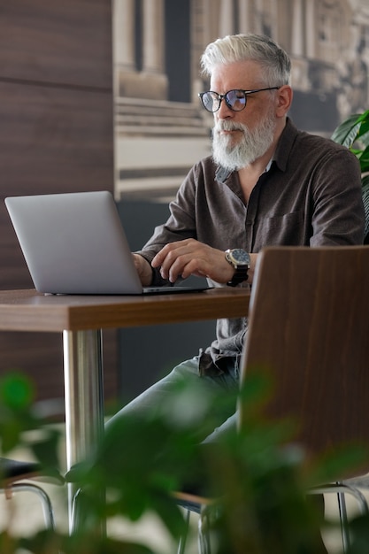 Een ongelooflijk mooie en stijlvolle grijsharige man van vijftig jaar die met een laptop werkt