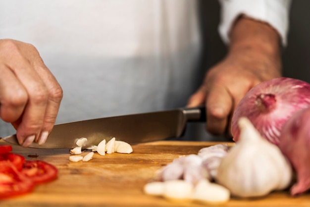 Een onherkenbare volwassen vrouw die beide handen op een keukenmes gebruikt om een knoflook op een snijplank te hakken voor de bereiding van lasagne