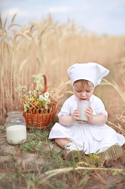 Een onschuldige baby zit met een glas verse koemelk op de grond in een veld