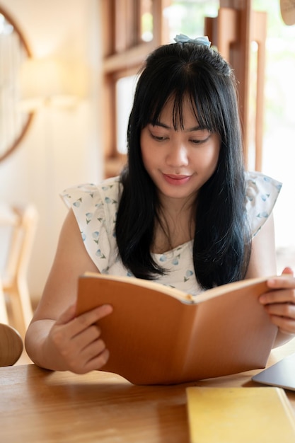 Een ontspannen en positieve jonge Aziatische vrouw die op een heldere dag een boek leest in een mooie koffieshop