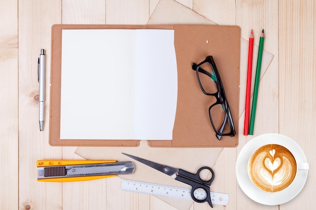 Een open blanco notitieboekje met kleurpotloden, pennen en kopje koffie op houten tafel