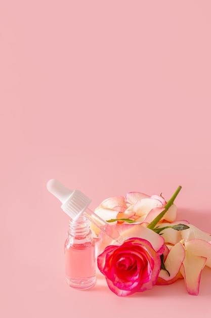 Een open cosmetische fles met pipetgevulde rozenolie op een roze bloem achtergrond Verticale weergave Een kopie ruimte natuurlijke cosmetica