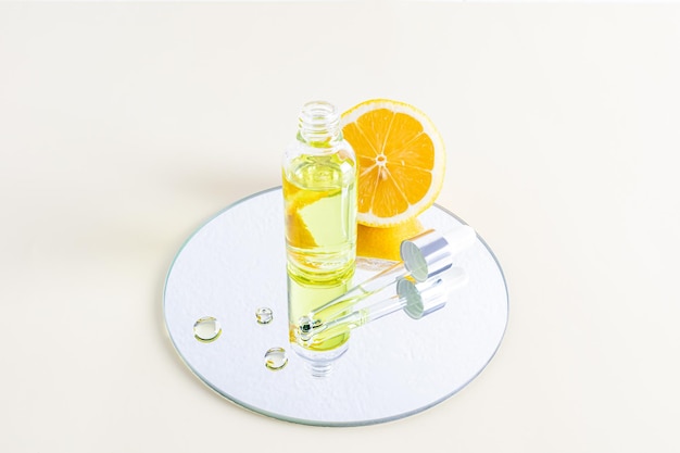 Een open glazen fles staat op een spiegel met een schijfje sappige citroen en een pipet gevuld met een natuurlijke cosmetica een serum op basis van citroenolie