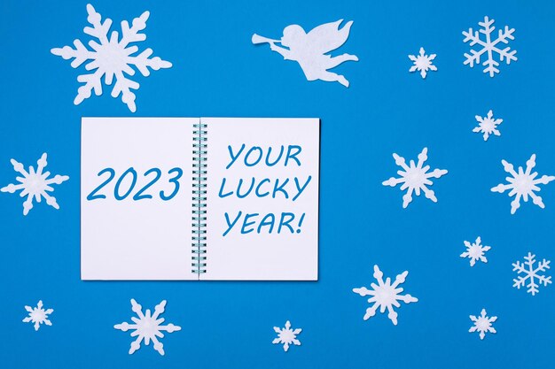Een open notitieboekje met de tekst 2023 en UW LUCKY YEAR op een blauwe achtergrond met kerstsneeuwvlokken