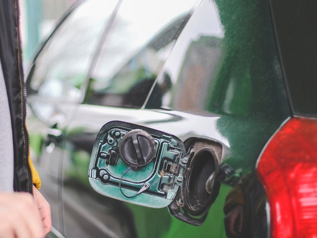 Een open tankdop op een groene auto met een rood achterlicht bij een benzinestation