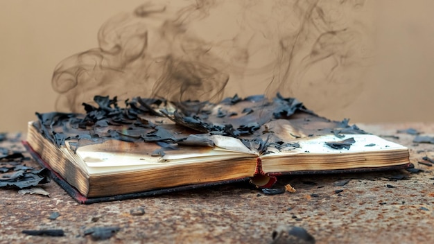 Een opengeslagen boek met verkoolde pagina's en rook boven het boek Verbrand boek tijdens een brand