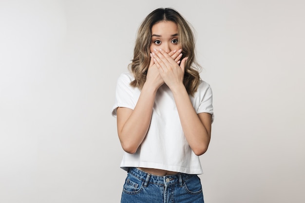 Een opgewonden geschokte emotionele schattige jonge vrouw poseren geïsoleerd over een witte muur wandbekleding mond