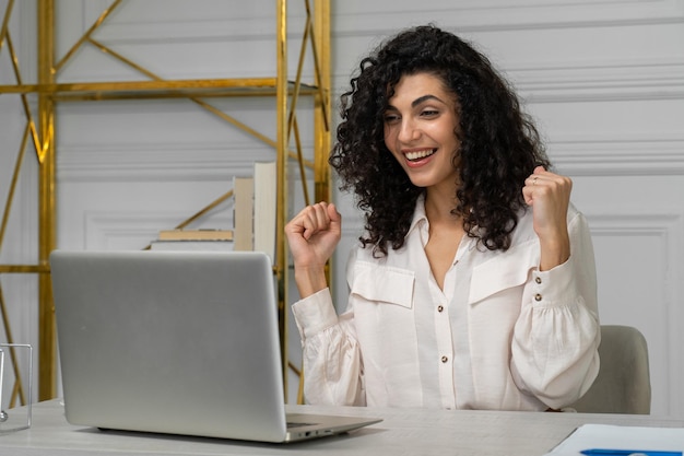 Een opgewonden Indiase werknemer kijkt naar het scherm van de laptop en leest het goede nieuws van een gelukkige jonge etnische vrouw