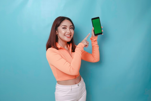 Een opgewonden jonge vrouw wijzend op kopieerruimte op haar smartphone in haar hand geïsoleerd op blauwe achtergrond