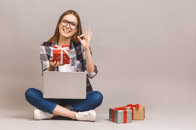 Een opgewonden toevallig meisje met laptopcomputer zittend op een vloer met stapel geschenkdozen