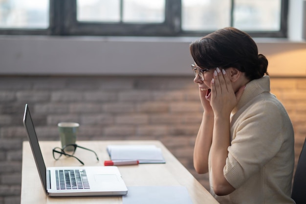 Een opgewonden vrouw die achter de laptop zit en er verbaasd uitziet