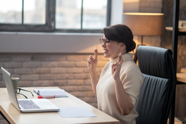 Een opgewonden vrouw die met gekruiste vingers achter de laptop zit