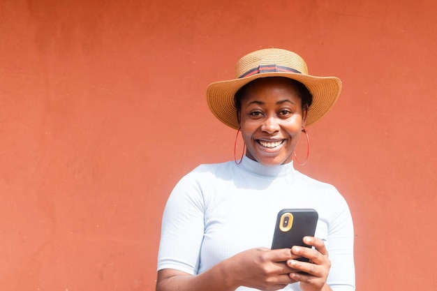 Een opwindend Afrikaans meisje dat lacht en naar de camera kijkt met een mobiele telefoon in de hand