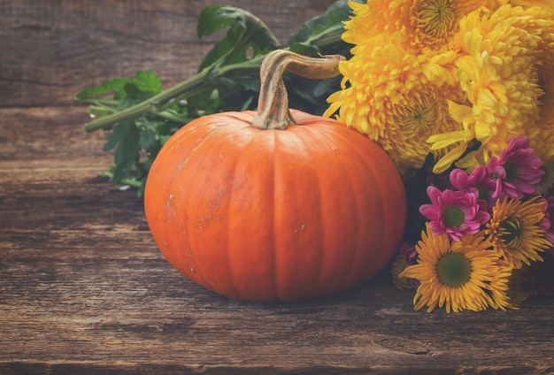 Een oranje pompoen met mama bloemen op houten getextureerde tafel, retro afgezwakt