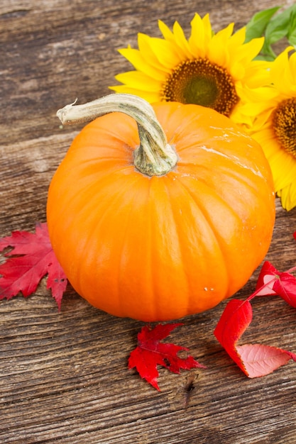 Een oranje pompoen met zonnebloemen en herfstbladeren op houten tafel