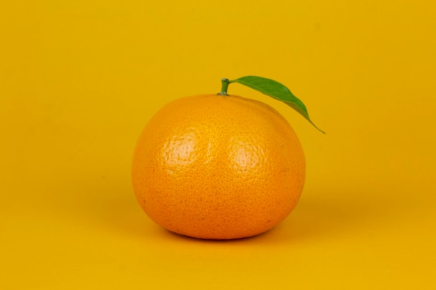 Een oranje vrucht met groen blad geïsoleerd op gele achtergrond Een oranje vrucht met blad stand