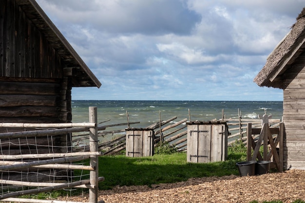 Een oud houten huis met een houten hek aan de rand van de zee en kleine visdrooghuizen in de m