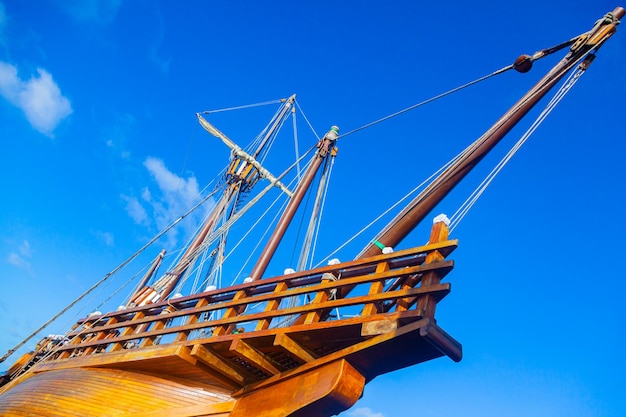 Een oud houten karveelschip met gevouwen zeilen tegen een blauwe lucht met witte wolken