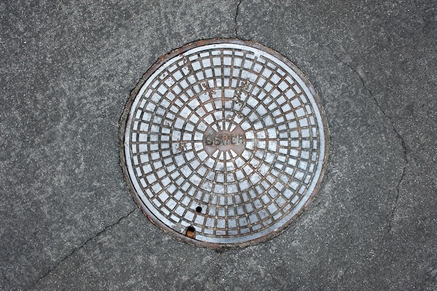 Een oud rioolputdeksel omgeven door een asfaltstraat