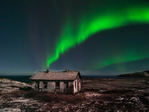 Een oud verlaten huis onder de noordelijke sterrenhemel. Nacht poollandschap met de Aurora Borealis.