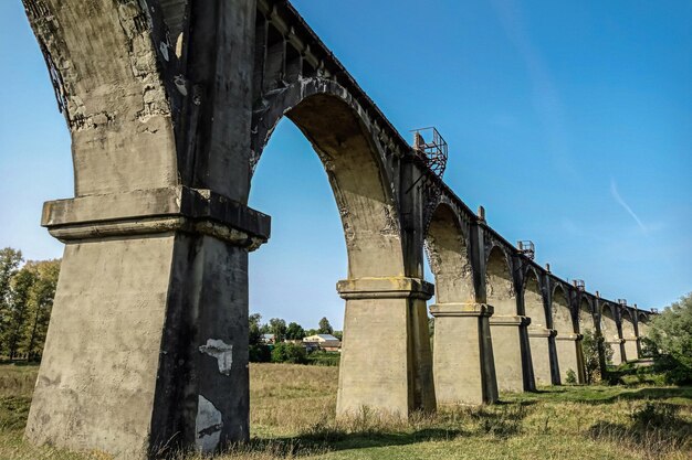 Een oud verlaten spoorbrugviaduct tegen de achtergrond van de lucht en het groene gras Mokrinsky Bridge