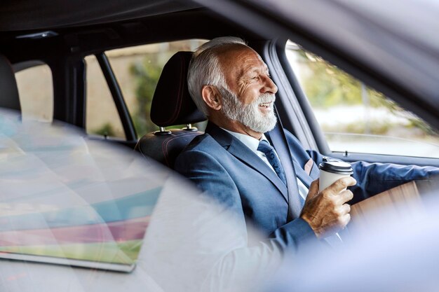 Foto een oude, bebaarde zakenman in pak rijdt met zijn auto naar zijn werk en drinkt zijn koffie to go