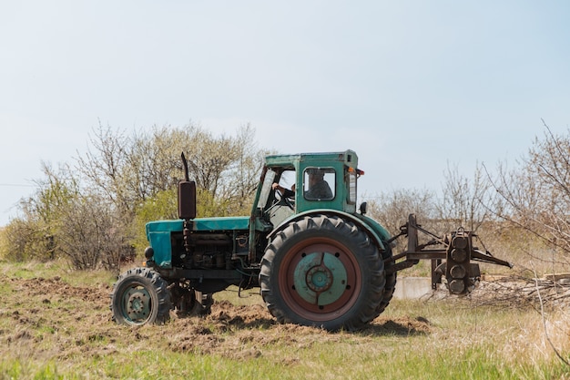 Een oude blauwe tractor ploegt een veld en bewerkt de grond.