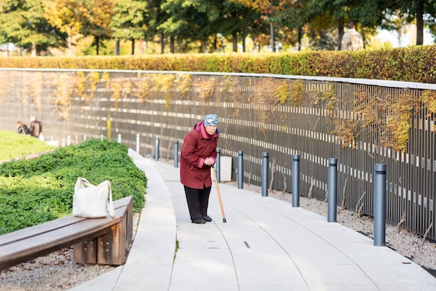 Een oude dame loopt in het park voorovergebogen gekleed in een rode jas