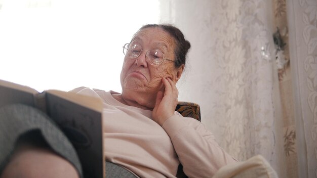 Een oude geïnteresseerde vrouw met een bril die in de fauteuil zit en een boek leest