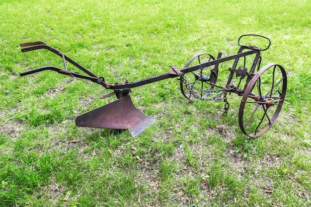 Een oude handgemaakte metalen ploeg met wielen staat op het veld. Een oud hulpmiddel om de grond te ploegen