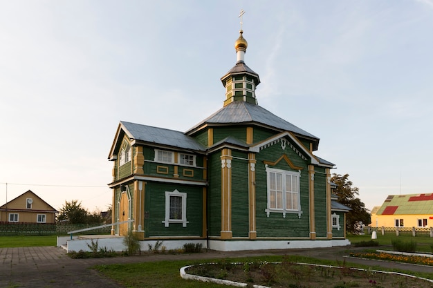 Een oude houten 19e-eeuwse kerk in groen met een gouden koepel en gouden kruis in warm zonlicht met een platform van groen gras