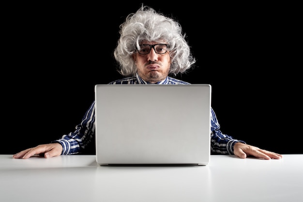 Een oude man boomer zittend op het bureau snuivend tijdens het gebruik van een computer-notebook op zwarte achtergrond