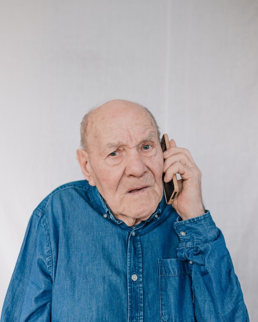 Een oude man in een blauw shirt zit en praat aan de telefoon