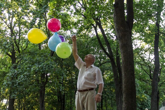 Een oude man speelt in het park met felgekleurde ballonnen op zijn verjaardag