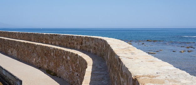 Een oude oude muur met heldere blauwe lucht en wazige zee op de achtergrond in Chania.