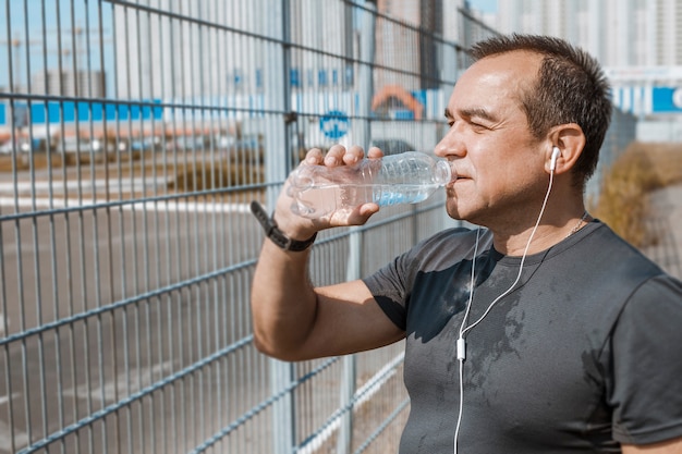 Een oude oudere man drinkt water tijdens het hardlopen.