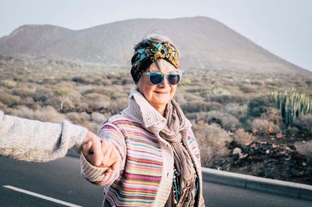 Een oude, oudere, vrolijke vrouw met gekleurde trendy kleding loopt in de buitenlucht, hand in hand met de man