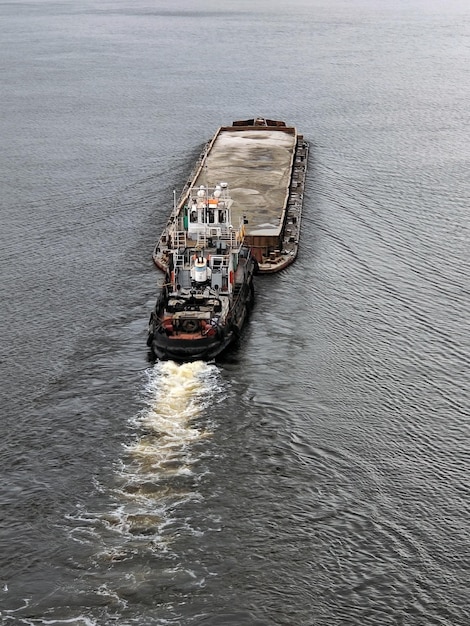 Een oude sleepboot duwt een bak met zand ervoor en drijft de rivier af Uitzicht van bovenaf