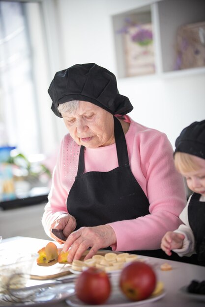 Een oude vrouw die een appel aan stukken snijdt met een klein meisje in de keuken