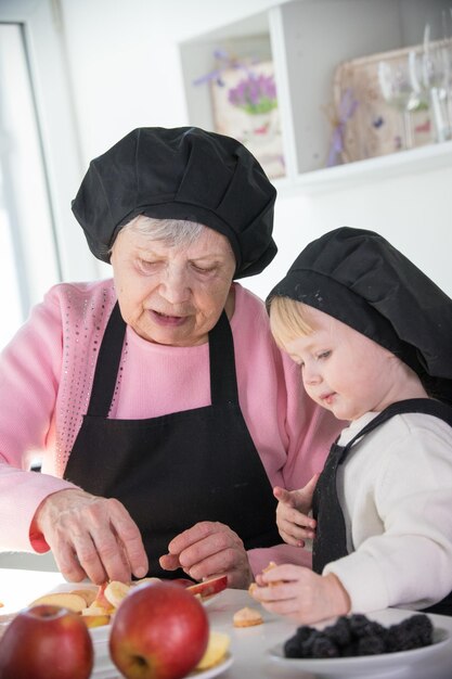 Een oude vrouw met een klein meisje dat in de keuken staat en fruit klaarmaakt voor een portie