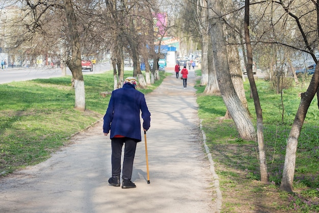 Een oude vrouw met stok loopt over straat. Oma heeft hulp nodig