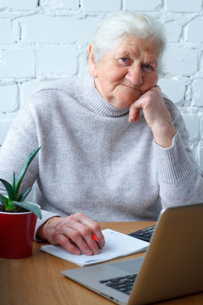 Een oude vrouw zit aan de tafel voor de laptop.