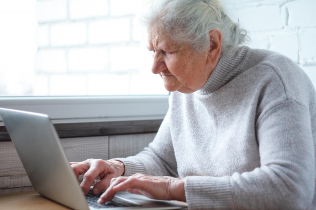 Een oude vrouw zit aan de tafel voor de laptop.