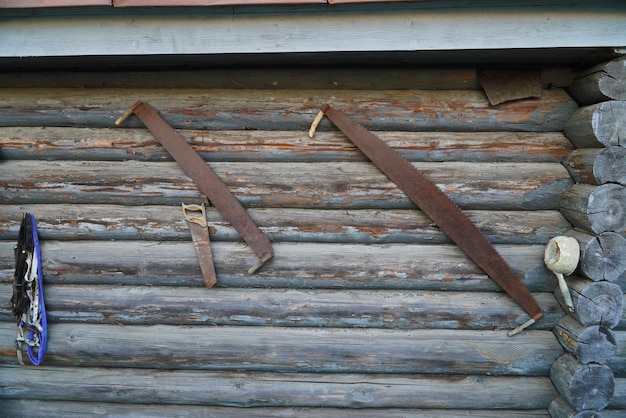 Een oude zaag met twee handen hangt aan een houten muur van boomstammen