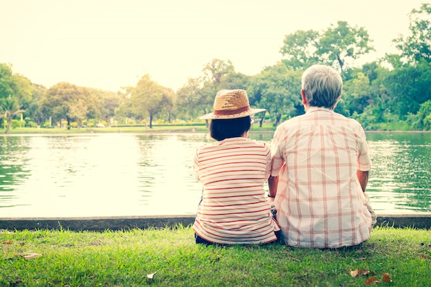 Een ouder echtpaar knuffelen elkaar met liefde en geluk in een park met een grote vijver.