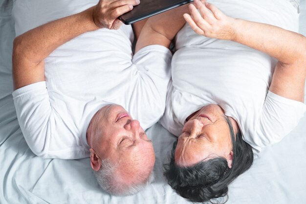 Een ouder echtpaar ligt in bed en gebruikt de tablet. senioren online