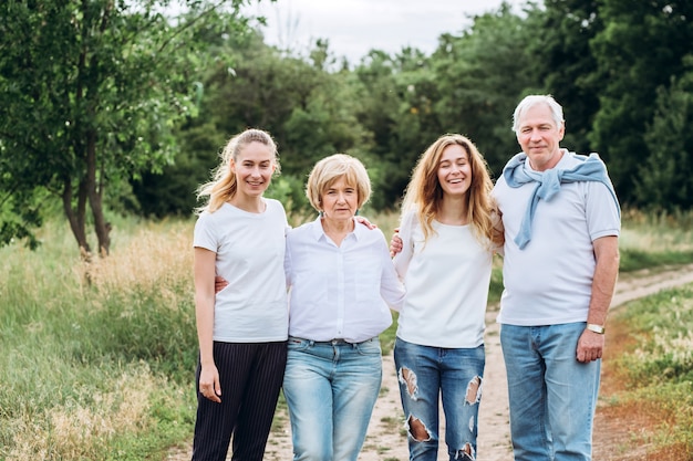 Een ouder echtpaar loopt met volwassen dochters in de natuur. Ouder paar wandelingen in het bos. Een familie in witte t-shirts en spijkerbroek loopt in het park. Gelukkig gezin. familie communiceert buitenshuis